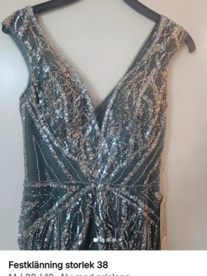 Glittrig blå långklänning med paljetter - Snygg blå långklänning med v-ringning och massor av silverfärgade paljetter som ger ett riktigt glittrigt intryck. Klänningen har ärmlös design och omlott-look framtill. Perfekt för dig som vill sticka ut på festen eller balen.