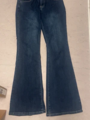 Blå utsvängda jeans - Säljer ett par blå jeans med utsvängda ben och klassisk femficksdesign. Jeansen har en hög midja och är tillverkade i denim. Perfekta för dig som gillar retrostil och vill ha ett par snygga och bekväma jeans.