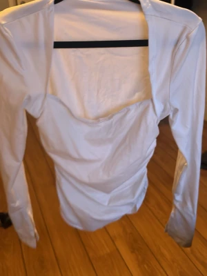 Vit långärmad topp med öppen rygg - Snygg vit långärmad topp med öppen rygg och figurnära passform. Toppen har en stilren design och är perfekt för att skapa en trendig look. Tillverkad i ett mjukt och stretchigt material som känns bekvämt mot huden.