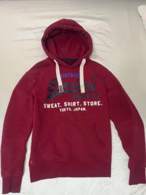Superdry hoodie Vinröd - Säljer en knappt använd vinröd superdry hoodie, hittar inte storleken men jag är 185 o den passar mig perfekt, skulle gissa på att den är M