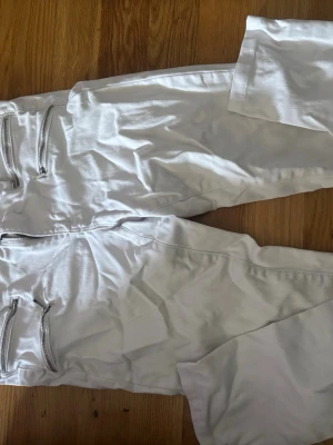 Vita jeans med dragkedjor fram - Säljer ett par vita jeans med smal passform och coola dragkedjor framtill. Jeansen har klassiska bakfickor och bälteshällor. Perfekta för dig som vill sticka ut med en fräsch och modern look.