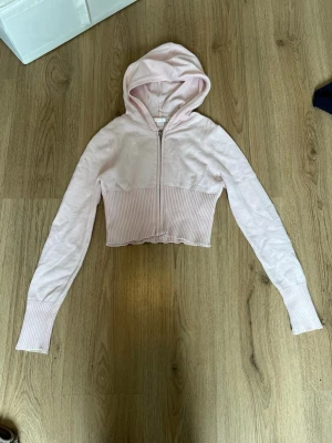 Ljusrosa cropped hoodie från Gina Tricot - Säljer en ljusrosa cropped hoodie från Gina Tricot med dragkedja framtill. Hoodien har långa ärmar, ribbade muddar och midja samt en mysig huva. Perfekt för en chill och trendig look.