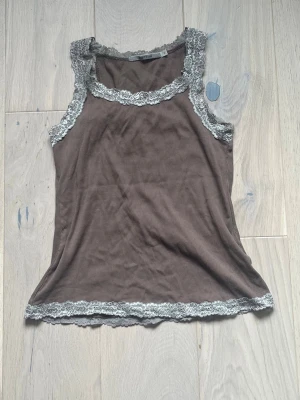 Y2k spets topp från Rosebud - Söt brun topp från Rosebud med fin spetskant runt halsringning, ärmhålor och nederkant. Material: 100 % bomull. Storlek M. Passar bra både till vardags och som ett lager under andra plagg. Använt skick men inga tydliga defekter