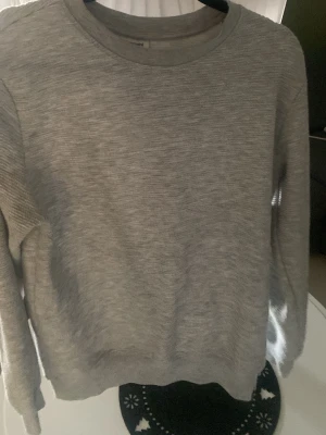 Grå stickad tröja från Kappahl  - En stilren grå stickad tröja med rund halsringning och långa ärmar. Tröjan har en enkel design utan mönster och ribbstickade muddar vid ärmslut och nederkant. Perfekt för lager-på-lager och passar till det mesta.