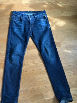 Mörkblå slim fit replay jeans - Snygga mörkblå slim fit jeans med klassisk femficksdesign och lätt slitning på låren. Jeansen har normal midja och raka ben, perfekta för en trendig och avslappnad look. Materialet är mjukt och stretchigt för extra komfort. Replay Wallys nypris 899 kr. Passar 170-178cm. Xs-S.