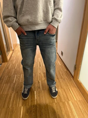 Blå raka jeans med tvättad look - Säljer ett par blå jeans med rak passform och snyggt tvättad finish. Jeansen har klassiska fem fickor och normal midja. Perfekta till sneakers och hoodie för en avslappnad stil.