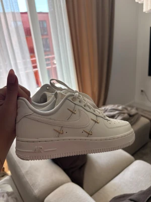 Nike Air Force 1 vita med gulddetaljer - Snygga vita Nike Air Force 1 sneakers med unika gulddetaljer på sidorna och klassisk swoosh. HELT NYA, använda 1 gång