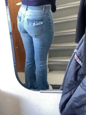 Ljusblå bootcut jeans med fickdetalj - Säljer ett par ljusblå bootcut jeans med snygga fickdetaljer bak och klassisk femficksdesign. Jeansen har normalhög midja och är i stretchigt denimtyg som sitter tajt över höfterna och låren. Orginal pris 600kr