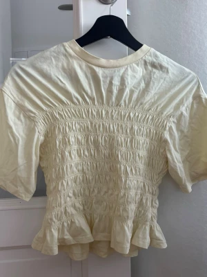 T shirt med smock - Supersöt ljusgul t-shirt från Gina Tricot med smockad midja och volangkant nedtill. Endast använd ett fåtal gånger.