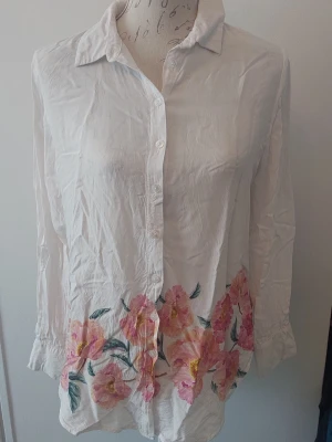 Blus med blomkant nedtill - Vit blus med blomkant nedtill i rosafärger. Blus I viskos.