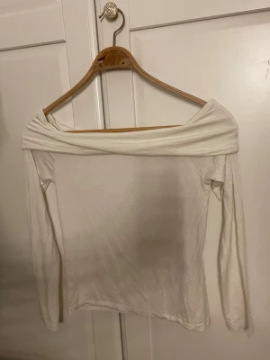 Vit off shoulder topp från 157 - Säljer en vit off shoulder topp från 157 i storlek XS. Toppen har långa ärmar och en bred, vikt kant över axlarna som ger en snygg och trendig look. Materialet är mjukt och stretchigt, perfekt för att styla med jeans eller kjol.