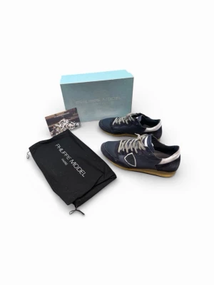 Philippe Model blå sneakers - Snygga blå sneakers från Philippe Model med vita detaljer och grå skosnören. Skorna har en klassisk låg siluett och en beige sula. Materialmix av mocka och textil ger en trendig look. Perfekta för dig som gillar stilrena och moderna sneakers.