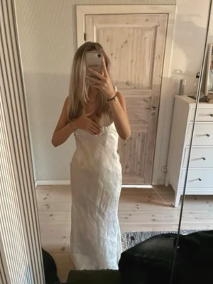 Beige balklänning  - Pris kan diskuteras vid snabb affär! Säljer en elegant vit långklänning med djup v-ringning och ärmlös design. Klänningen har en figurnära passform och är tillverkad i ett lätt, mjukt material som ger en lyxig känsla. Perfekt för dig som vill ha en stilren och trendig look.