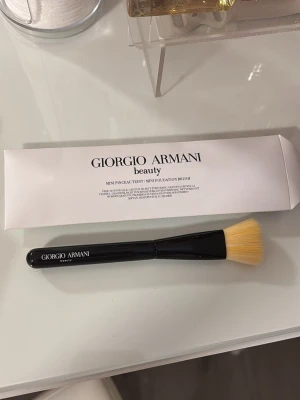 Giorgio Armani  foundationborste - Snygg mini foundationborste från Giorgio Armani med svart handtag och täta, ljusgula borst. Perfekt för att applicera flytande foundation jämnt och smidigt. Kommer i originalförpackning och har en stilren design som känns lyxig.