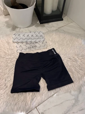 Midnight black impact 4.5 DFYNE - Säljer ett par svarta träningstights shorts från DFYNE med hög midja och tight passform. Perfekta för gymmet eller löprundan. Materialet är stretchigt och bekvämt, och loggan syns framtill i midjan.