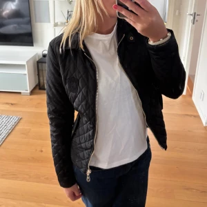 Svart quiltad jacka från Massimo Dutti - Snygg svart quiltad jacka från Massimo Dutti med guldfärgad dragkedja och diskret logga på bröstet. Jackan har lång ärm och en figurnära passform som ger en stilren look. Storlek S! 