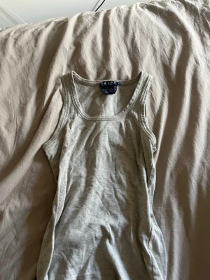 Grå linnetopp från Ralph Lauren - Snygg grå linnetopp från Ralph Lauren i 100% bomull. Klassisk och enkel design med rund halsringning och ärmlös passform. Perfekt att matcha med jeans eller shorts för en avslappnad look.
