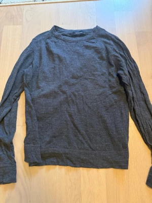 Mörkgrå tröja Peak Performance XL - En stilren mörkgrå långärmad tröja från Peak Performance. Tröjan har rund halsringning och är tillverkad i ett mjukt, tunt material som passar perfekt för lager-på-lager. Enkel design utan tryck eller mönster.