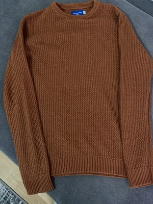 Brun stickad tröja från Jack & Jones - Säljer en brun stickad tröja från Jack & Jones Originals med rund halsringning och grovstickad struktur. Tröjan har långa ärmar och ribbade muddar vid ärmslut och nederkant. Perfekt för kyliga dagar och enkel att matcha.