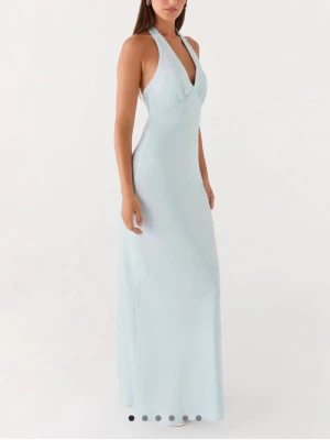 Ljusblå långklänning med knyt - Elegant ljusblå långklänning med halterneck och knyt i nacken samt ryggen. Klänningen har en öppen rygg och är ärmlös, vilket ger en stilren och modern look. Tillverkad i ett mjukt, lätt material som faller snyggt längs kroppen.