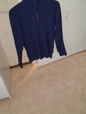 Mörkblå stickad tröja med halv dragkedja - Mörkblå stickad tröja med hög krage och halv dragkedja framtill. Tröjan har långa ärmar och ribbade muddar vid ärmslut och nederkant. Perfekt för lager på lager och enkel att matcha till olika outfits.