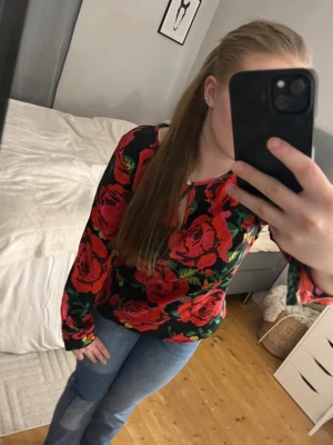 Blommig långärmad blus med rosor - Snygg blus med stora röda och rosa rosor på svart botten. Blusen har lång ärm och en lätt v-ringning. Materialet ser ut att vara mjukt och följsamt, perfekt för dig som gillar färgstarka mönster och vill sticka ut lite extra. Säljer också jeansen! 