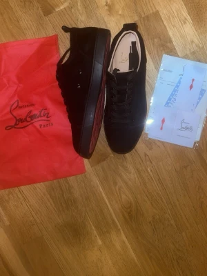 Svarta Louboutin sneakers med röd sula - Säljer ett par svarta sneakers från Christian Louboutin med den ikoniska röda sulan. Skorna har lågt skaft, svarta skosnören och är tillverkade i mocka. Medföljer påse och certifikat. Perfekta för dig som vill ha något exklusivt och stilrent. Pris kan diskuterades. Det bara att ställa frågor vid intresse😁