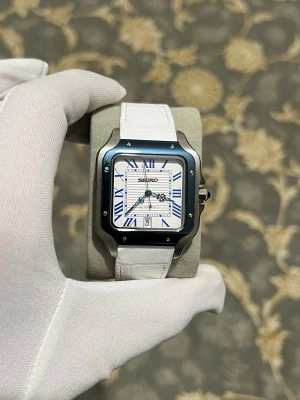 Seiko mod Santos automatic  - Stilren Seiko-klocka med fyrkantigt silverfärgat boett, vit urtavla med blå romerska siffror och datumvisning. Klockan har en vit läderrem med krokodilmönster och klassiskt spänne. Perfekt accessoar för dig som gillar en modern och elegant look.