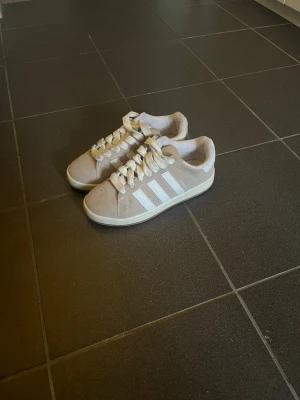 Beige Adidas sneakers med vita ränder -  Köpte dom snabbt då jag var behov av ett par skor men säljer dom nu då dom inte används. Kan gå ner i pris vid snabb affär vill bli av med dom fort!