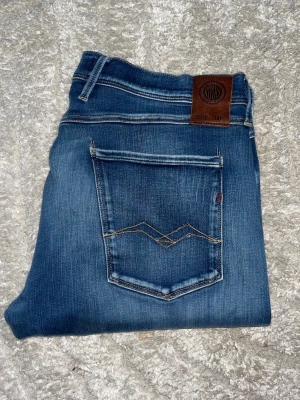 Replay Anbass jeans  - Snygga blå slim fit jeans från Replay med klassisk femficksdesign och dekorativa sömmar på bakfickan. Jeansen har en något tvättad look och är tillverkade i stretchigt denimtyg för extra komfort. (Se hål på ena knäet) JAG SKICKAR EJ FLER BILDER PÅ JEANSEN! för storleksguide hänvisar jag till måtten och för bättre inblick i passformen rekommenderar jag att googla på modellnamnet. :) 1,107 