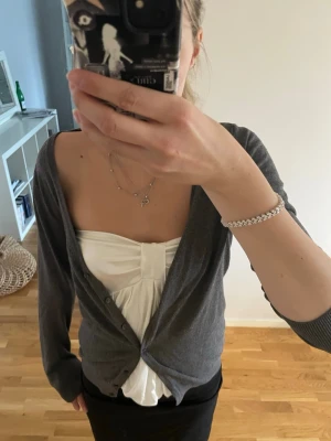 Mörkgrå kofta med knappar - En stilren mörkgrå kofta med knäppning framtill. Koftan har en klassisk passform med långa ärmar och ribbade muddar. Perfekt att slänga över en topp för en avslappnad look.