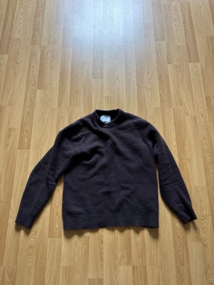 Mörkbrun merinoullströja Vaillent - Säljer en enkel och stilren mörkbrun stickad tröja från Vaillent i mjuk merinoull. Tröjan har rund halsringning och långa ärmar, perfekt för lager på lager under kyliga dagar. Passar dig som gillar minimalistisk och klassisk stil.