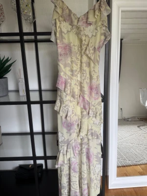 Lång blommig volangklänning - Långklänning med volanger och blommigt mönster, v-ringad. 