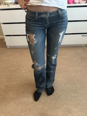 Blå slitna bootcut jeans från Guess. Skicka gärna prisförslag som ni tycker är rättvist så kan vi fixa något 🩷 - Säljer ett par blå bootcut jeans från Guess med coola slitningar och hål på benen. Jeansen har klassisk femficksdesign, låg midja och är gjorda i denim. Perfekta för dig som har storlek xs eller s i jeans. Finns en liten slitning på bält flärpen men det går att sy fast själv🩷