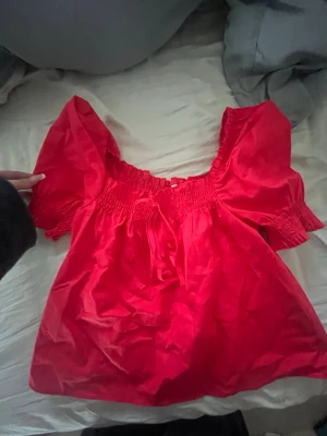 Röd puffärm blus med smock - Trendig röd blus med puffärmar och smockdetaljer vid axlar och midja. Toppen har en söt knytning framtill och är tillverkad i ett mjukt, lätt tyg som ger en luftig känsla. Perfekt och super fin om du ska åka utomlands eller nu till sommaren 😍