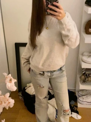 Beige oversized stickad tröja - Mysig beige stickad tröja med avslappnad passform och rund hals. Tröjan har långa ärmar och ribbade muddar vid ärmslut och nederkant. Perfekt för lager på lager och enkel att matcha med jeans eller kjol.