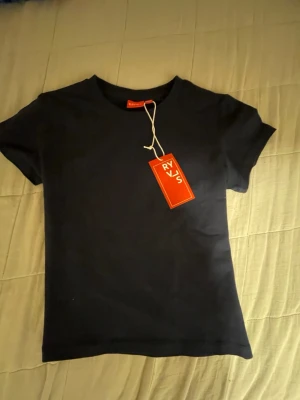 Svart t-shirt från RYVS - En stilren svart t-shirt från RYVS med klassisk rund hals och korta ärmar. Tillverkad i mjuk bomull för en skön känsla. Perfekt basplagg att matcha med allt. Tidlös design och enkel passform.