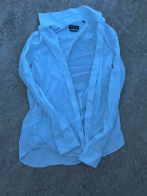 Vit klassisk skjorta från dressmann - Klassisk vit skjorta från dressmann med lång ärm och knappar framtill. Skjortan har en tidlös design med normal passform och är tillverkad i bomull för en skön känsla. Perfekt till både jeans och kostym.