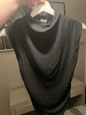 Svart ärmlös topp från Gina tricot  - Snygg svart topp från Weekday med draperad halsringning och ärmlös design. Tillverkad i mjukt bomullsmaterial som känns skönt mot huden. Perfekt att styla med jeans eller kjol för en clean look.