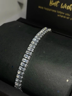 Silverfärgat tennisarmband med stenar - Ett stilrent tennisarmband i silverfärg med rektangulära, gnistrande stenar som sitter tätt i rad. Armbandet har en klassisk och elegant design som passar till många olika stilar. 