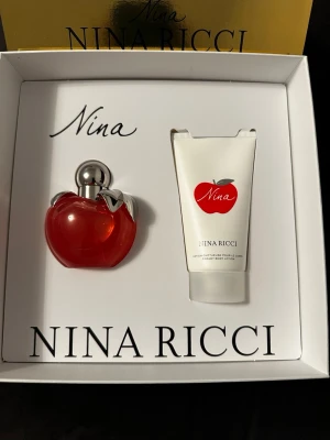 Nina Ricci Nina parfymset - Exklusivt parfymset från Nina Ricci med doften Nina. Setet innehåller en röd äppelformad parfymflaska med silverdetaljer och en matchande vit bodylotion med röd äppellogga. Allt levereras i en elegant vit och guld presentförpackning.                                             •Eau de toilette 50 ml •Bodylotion 75 ml. •Perfekt som studentgåva 🧡