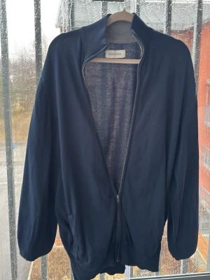 Mörkblå ziptröja från Pier one - Mörkblå ziptröja från Pier one med hög krage och ribbade muddar. Tröjan har två fickor framtill och är tillverkad i ett mjukt, tunt stickat material. Perfekt för lager på lager och enkel att matcha med olika outfits.