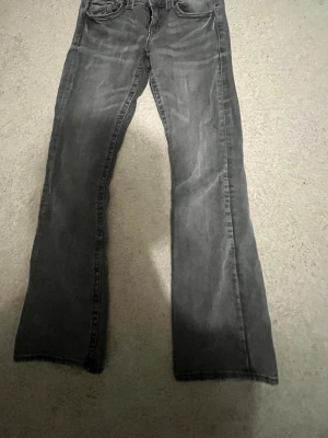 Grå bootcut jeans med slitningar - Säljer ett par grå jeans med bootcut passform och snygga slitningar. Säljer på grund av att den inte passar, två små fläckar där bakpå jeansen men syns knappt.