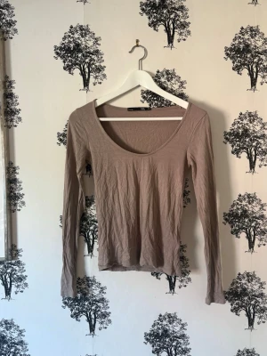 Beige långärmad topp med rund hals - En enkel och stilren beige långärmad topp med rund, djup ringning framtill. Tillverkad i mjukt bomullsmaterial som känns skönt mot huden. Perfekt att matcha med jeans eller kjol för en clean look.