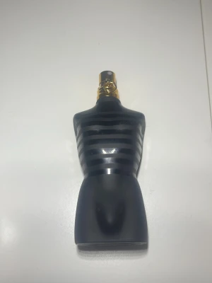 Jean Paul Gaultier Le Male parfym - Säljer en Jean Paul Gaultier Le Male parfym i en ikonisk flaska formad som en manlig torso. Flaskan är svart med horisontella ränder och har en guldfärgad spraytopp. Materialet är glas och designen är riktigt snygg och unik.