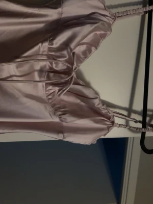 Ljusrosa långklänning i satin - Supersnygg ljusrosa långklänning i satin med smala axelband och en söt knytdetalj framtill. Klänningen har en elegant, slät siluett och ett glansigt material som ger en lyxig känsla. Perfekt för dig som vill sticka ut med en stilren look. Från bikbok och använd 1 gång vid bal❤️skriv om du har fler frågor