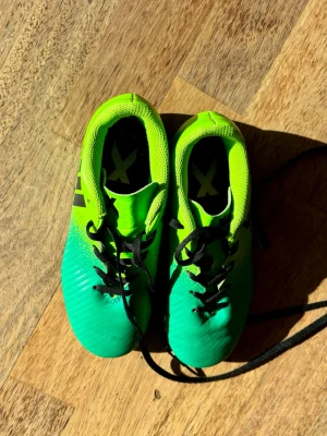 Neongröna Adidas fotbollsskor - Säljer ett par snygga neongröna Adidas fotbollsskor med svarta detaljer och snörning. Skorna har låg profil och är tillverkade i syntetmaterial för bra grepp och känsla på planen. Perfekta för dig som vill sticka ut på matchen!