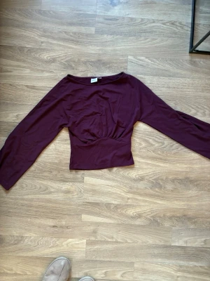 Mörkröd topp från Gina Tricot - Säljer en mörkröd långärmad topp från Gina Tricot. Toppen har en figurnära passform med markerad midja och bred halsringning. Använd bara 1 gång