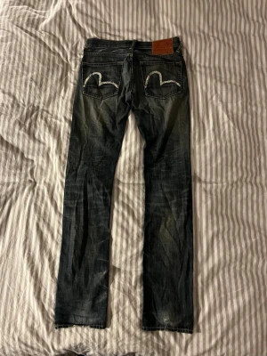 Washed Evisu Jeans 100% cotton - Ett par riktigt snygga Evisu Jeans från Japan. De har snygga fades och är 100% cotton.                                                     Jeansen har ett hål i högra fickan men det går att laga om man skulle vilja             Midja 39 cm                                                        längd 107 cm                                    Benöppning 17 cm                                                 Om ni undrar något är det bara att fråga!