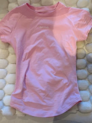 Rosa kortärmad t-shirt från DFYNE - Snygg ljusrosa t-shirt från DFYNE med korta ärmar och rund hals. Tillverkad i ett mjukt och stretchigt material som passar perfekt till träning eller chill. Diskret logga framtill i vitt. Enkel och stilren design.